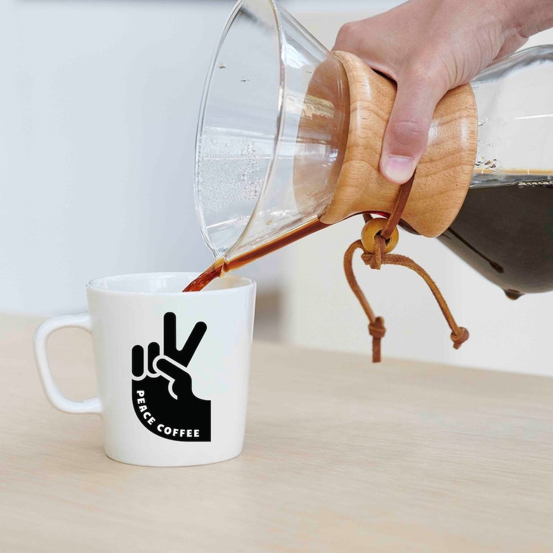 Pouring coffee from a Chemex-style brewer into a Peace Coffee mug