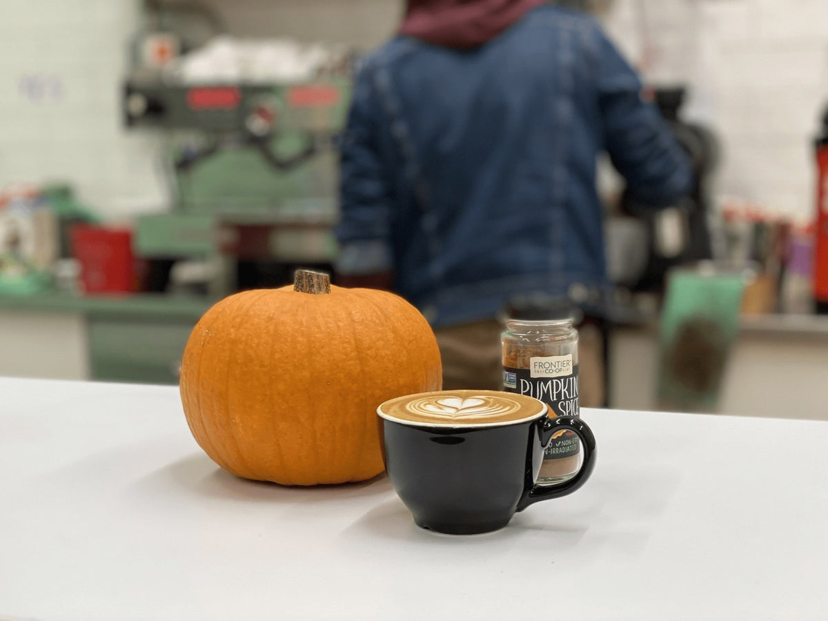 Pumpkin spice latte next to a pumpkin on the Peace Coffee cafe counter